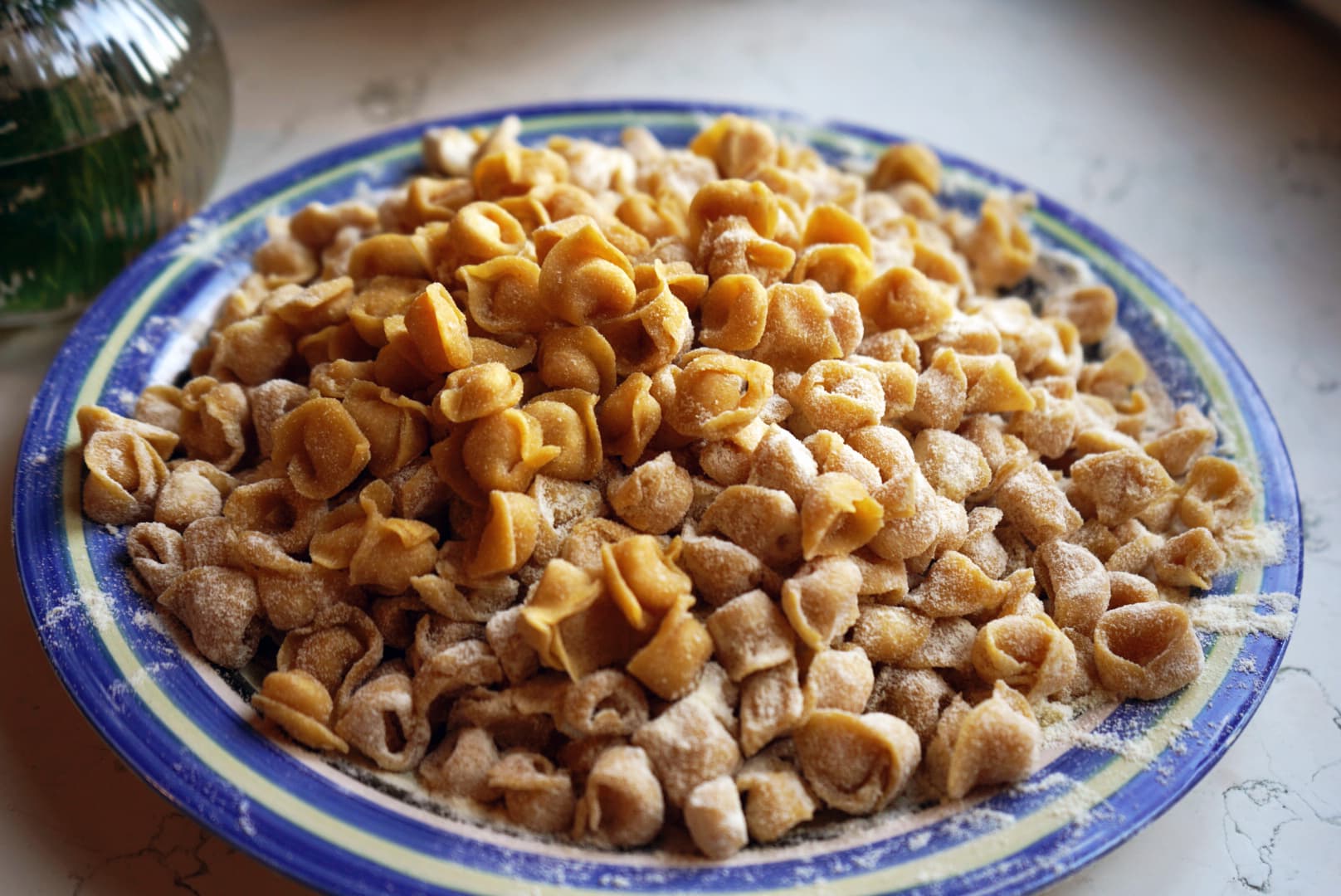 Tortellini fatti a mano spolverati di farina su un piatto decorato blu e bianco.