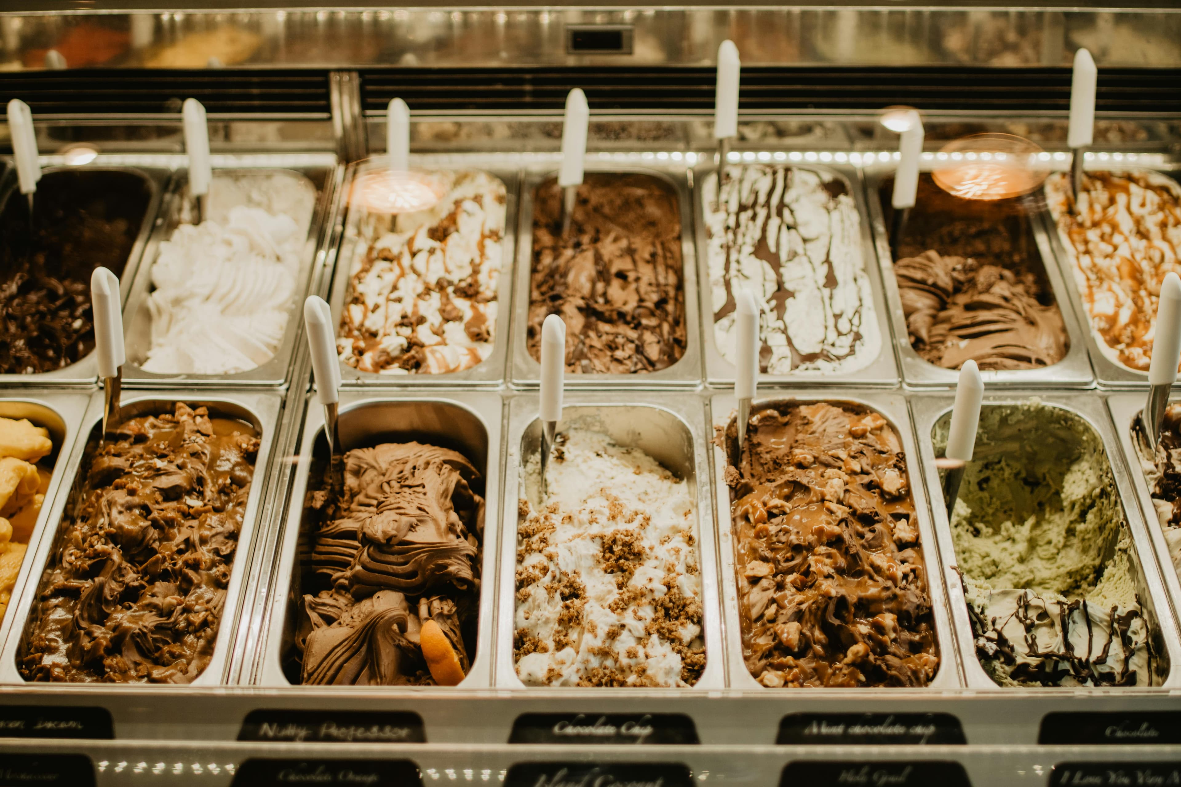 Assortimento di vari gusti di gelato artigianale in vaschette di metallo con spatole bianche.